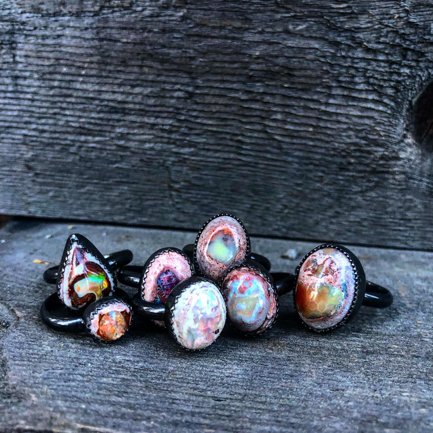 A cluster of fire opal rings in pink, lavender and amber tones on weathered wood