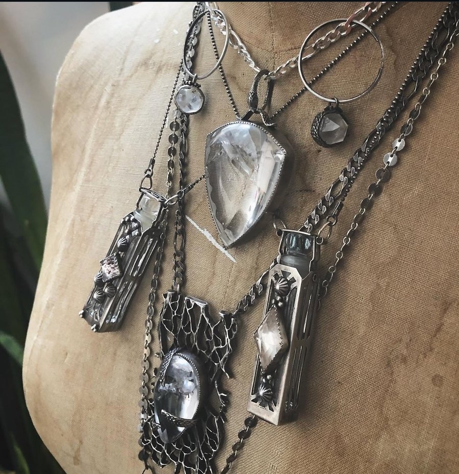 Layered sterling necklaces, phials and a large quartz pendant on a linen dress form