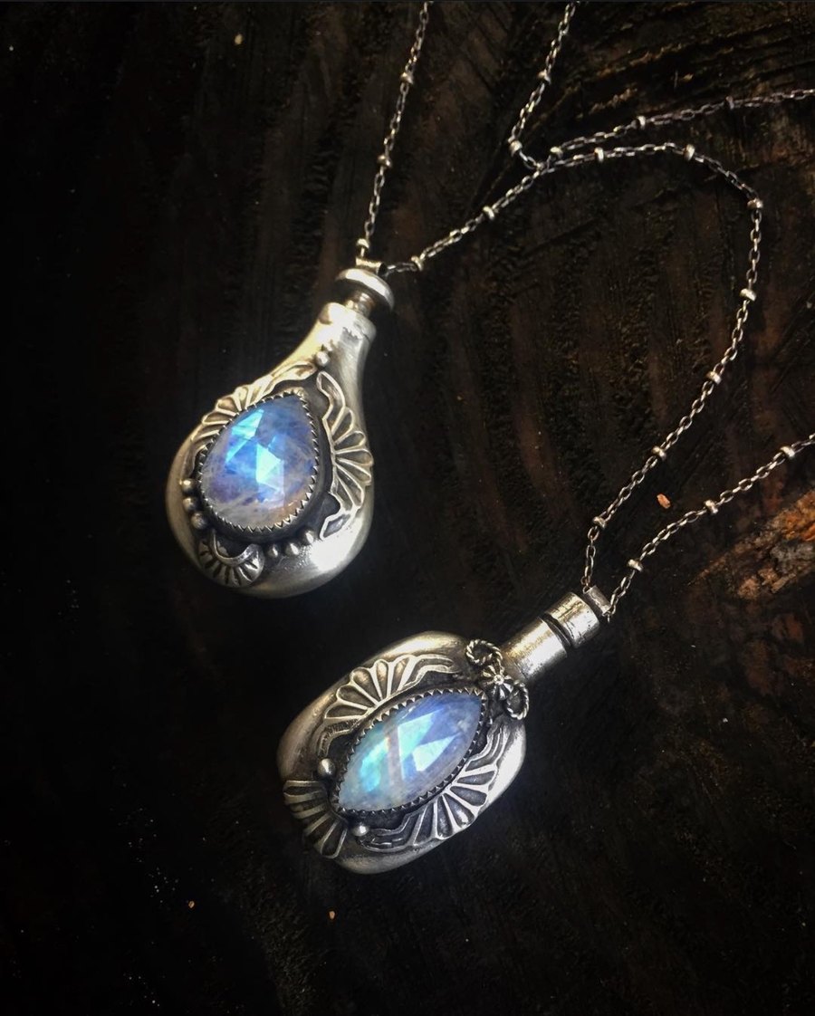 Two sterling moonstone perfume phial pendants on dark wood