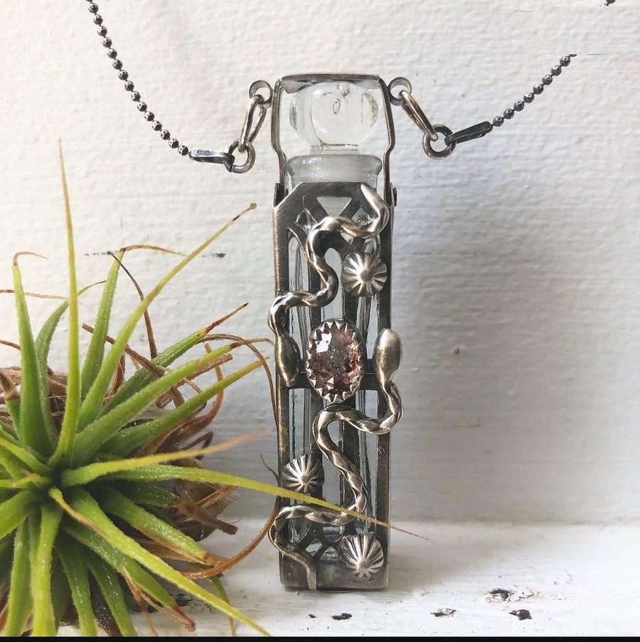 A sterling serpent potion phial with a Super 7 stone, hanging beside an air plant