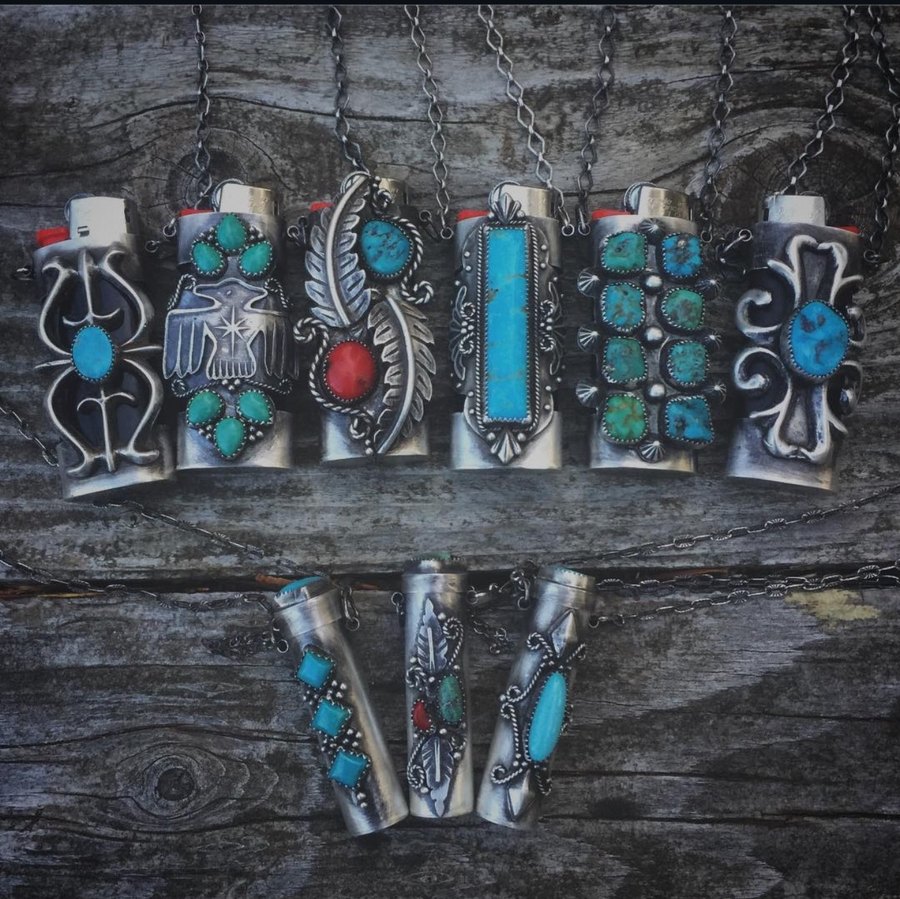 Nine sterling FireKeeper lighter cases with turquoise, coral and thunderbird designs hanging on weathered wood