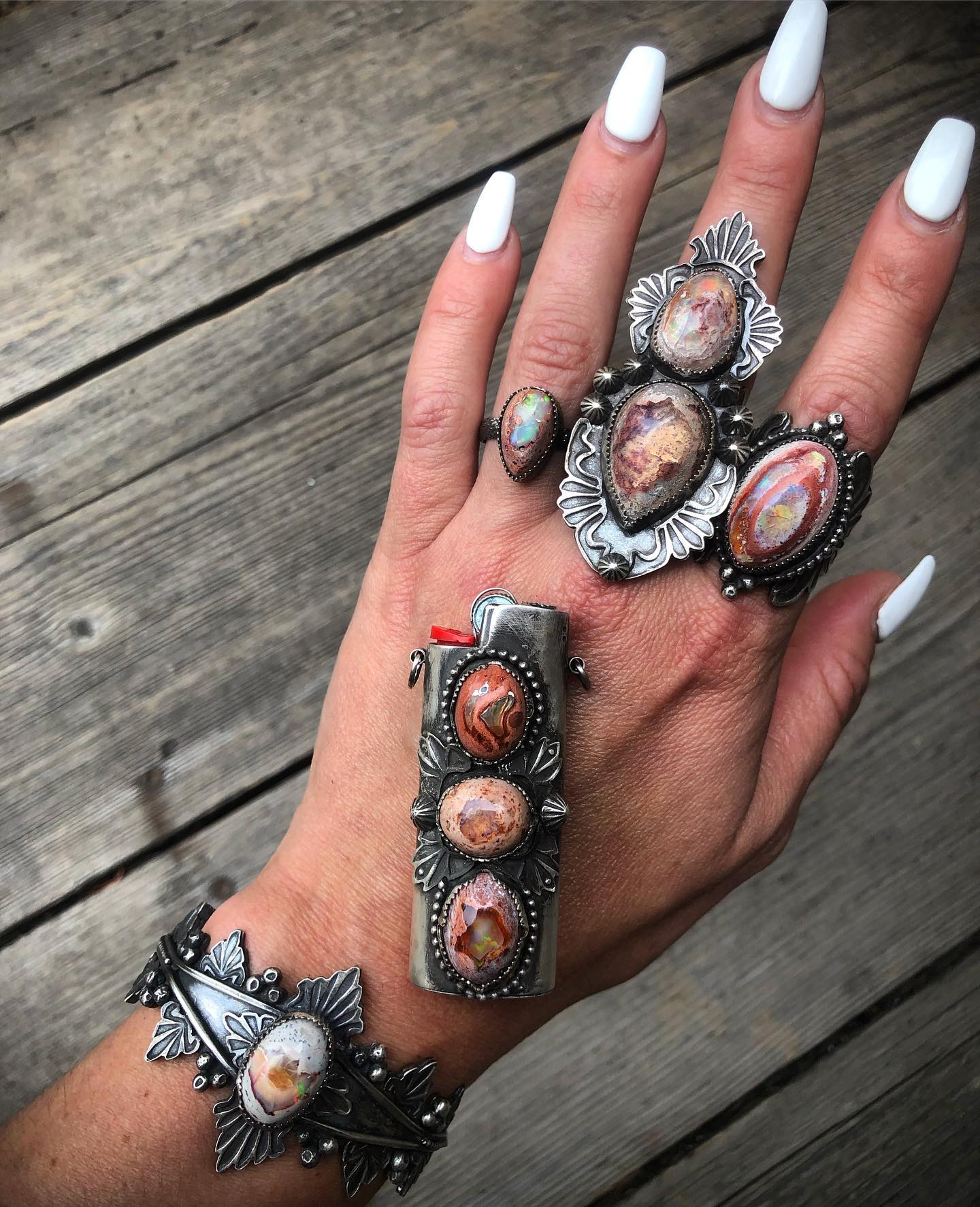 Jenna's hand wearing her fire opal rings, FireKeeper lighter case and opal cuff on weathered wood, 2019