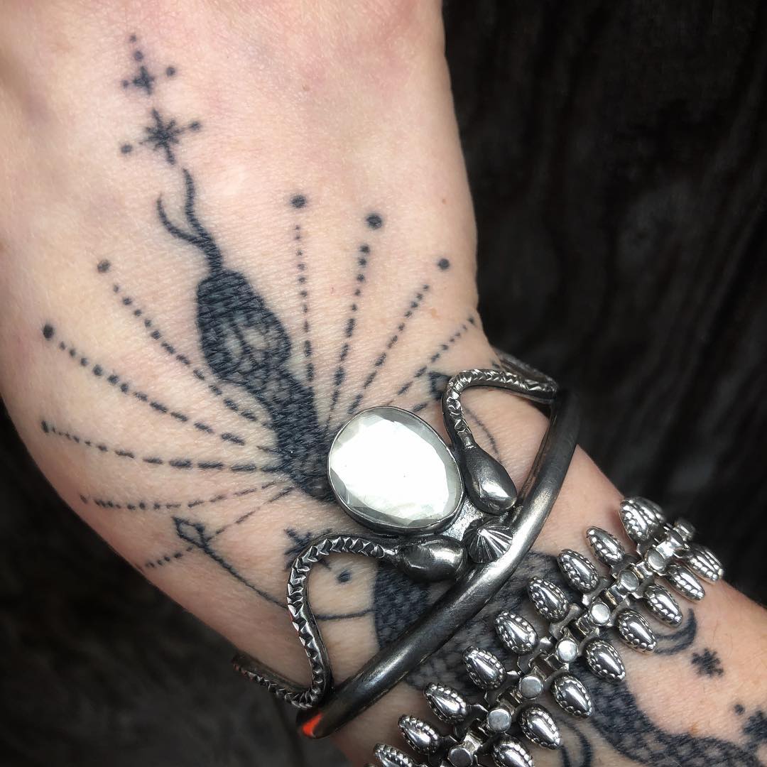 Jenna's tattooed wrist wearing a sterling snake cuff set with a large faceted stone, stacked with a beaded sterling bracelet