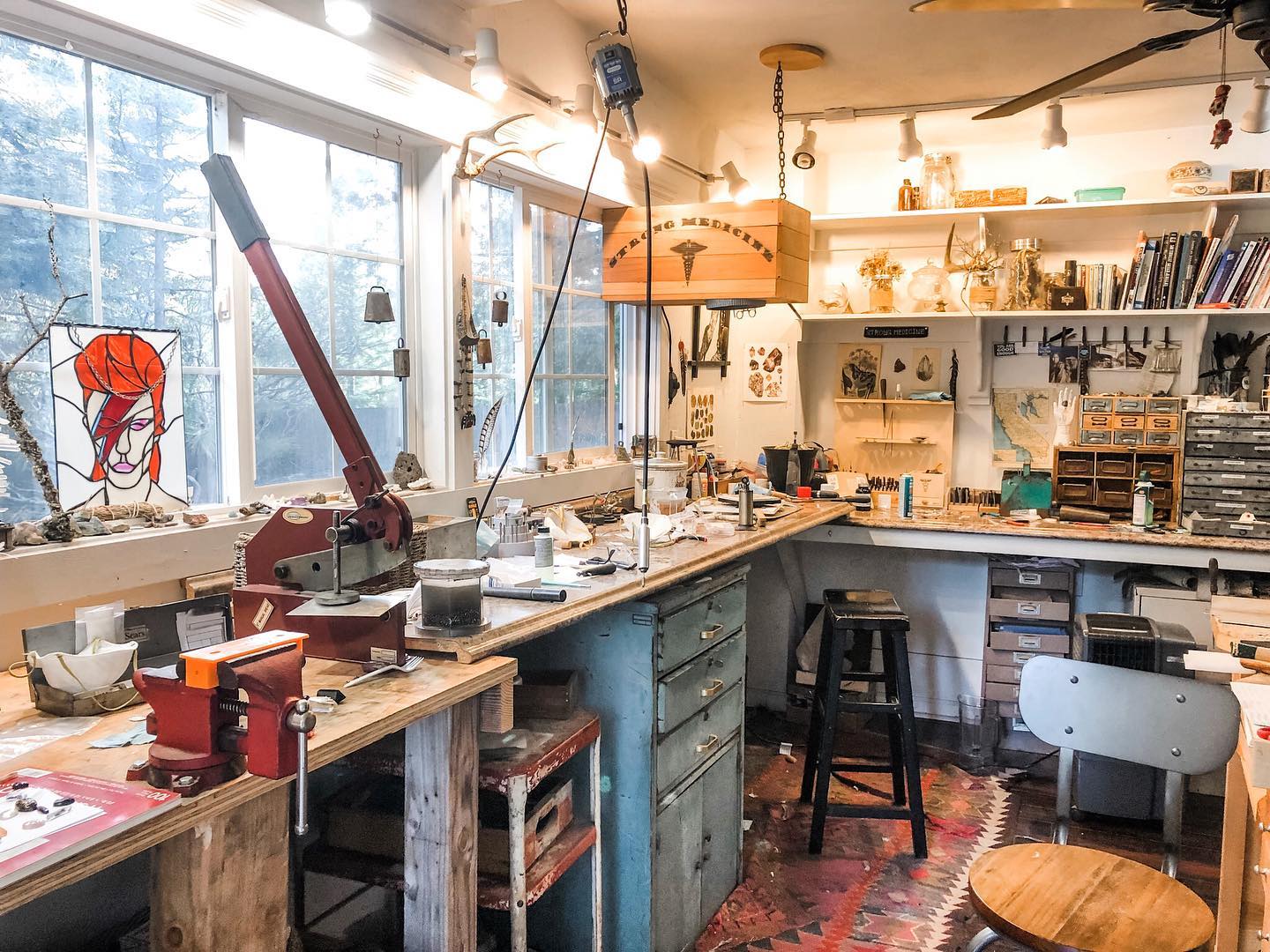Jenna's workbench: a long bench under tall windows, tools, presses, and a hanging wooden Strong Medicine sign